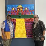 Two people standing on each side of a painting on the wall and smiling