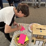 Lady bent over a table and writing on a bright pink notecard