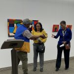 Three people standing with their backs to the art on the wall and smiling and talking
