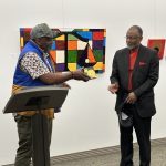 Two men standing in front of art in a gallery and going in for a handshake