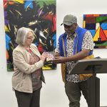 Two people standing in front of art in a gallery. One man standing in front of a podium.