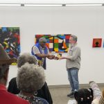 Two men standing in front of art in a gallery and shaking hands.