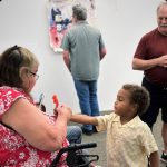 Woman talking to a little boy and a man looking at wall art in the background