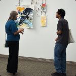 Two people standing looking at art on the wall in an art gallery