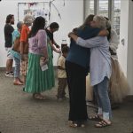 Women standing around in an art gallery. Two women hugging.
