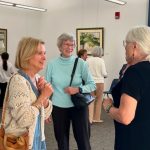 Three women standing in an art gallery and talking to each other