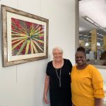 Jane Jackson with Deborah in an orange/yellow shirt standing next to art on the wall