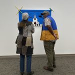 Two people with their backs to the camera while facing a piece of art on the wall