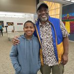Man and younger boy smiling and posing for the camera in an art gallery