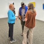 Three people standing in a circle in the middle of an art gallery