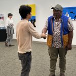 Man shaking hands with a younger guy in the middle of an art gallery