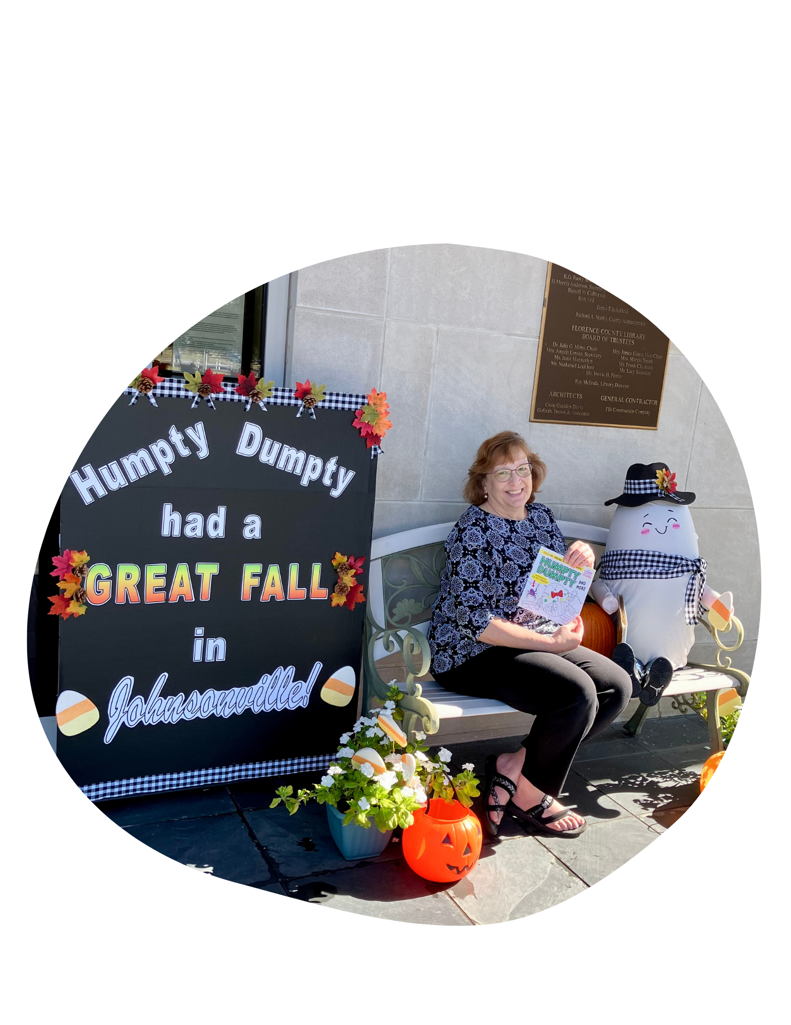 A lady sitting down on a bench next to Humpty Dumpty and a fall display