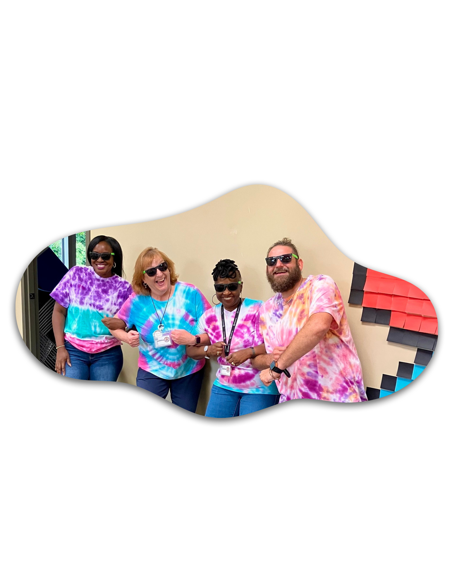 Three women and one male dressed in tye dye shirts with their arms interlocked