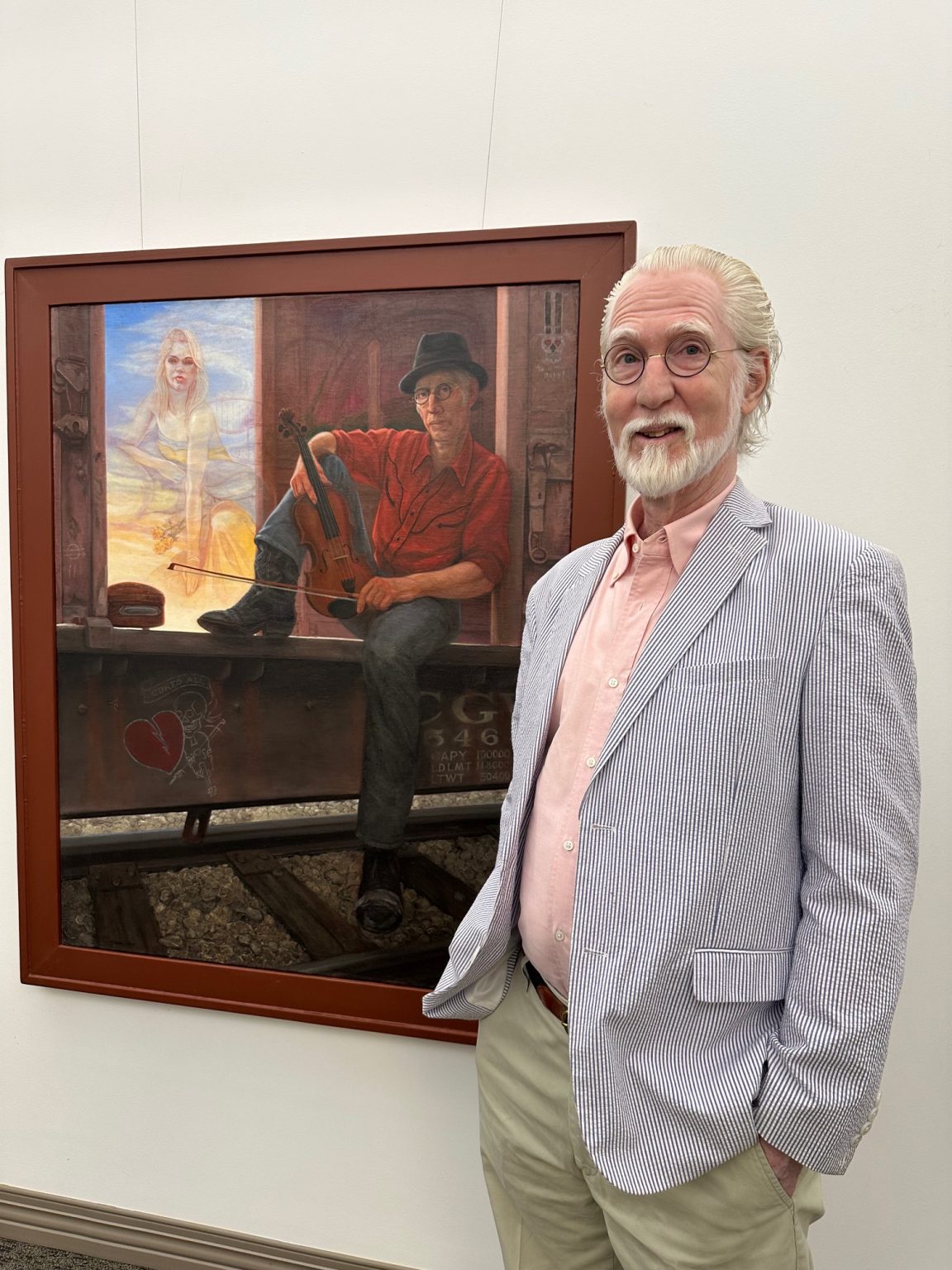 Picture of white haired male standing in front of self-portrait painting