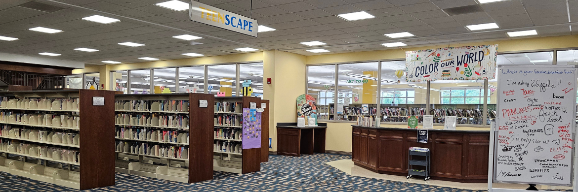 Photo of book shelves, desk, and white board in teen area of library