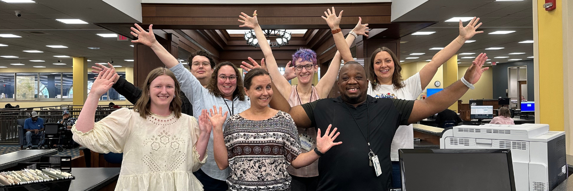 Group photo of adult services staff with smiles and hands in the air