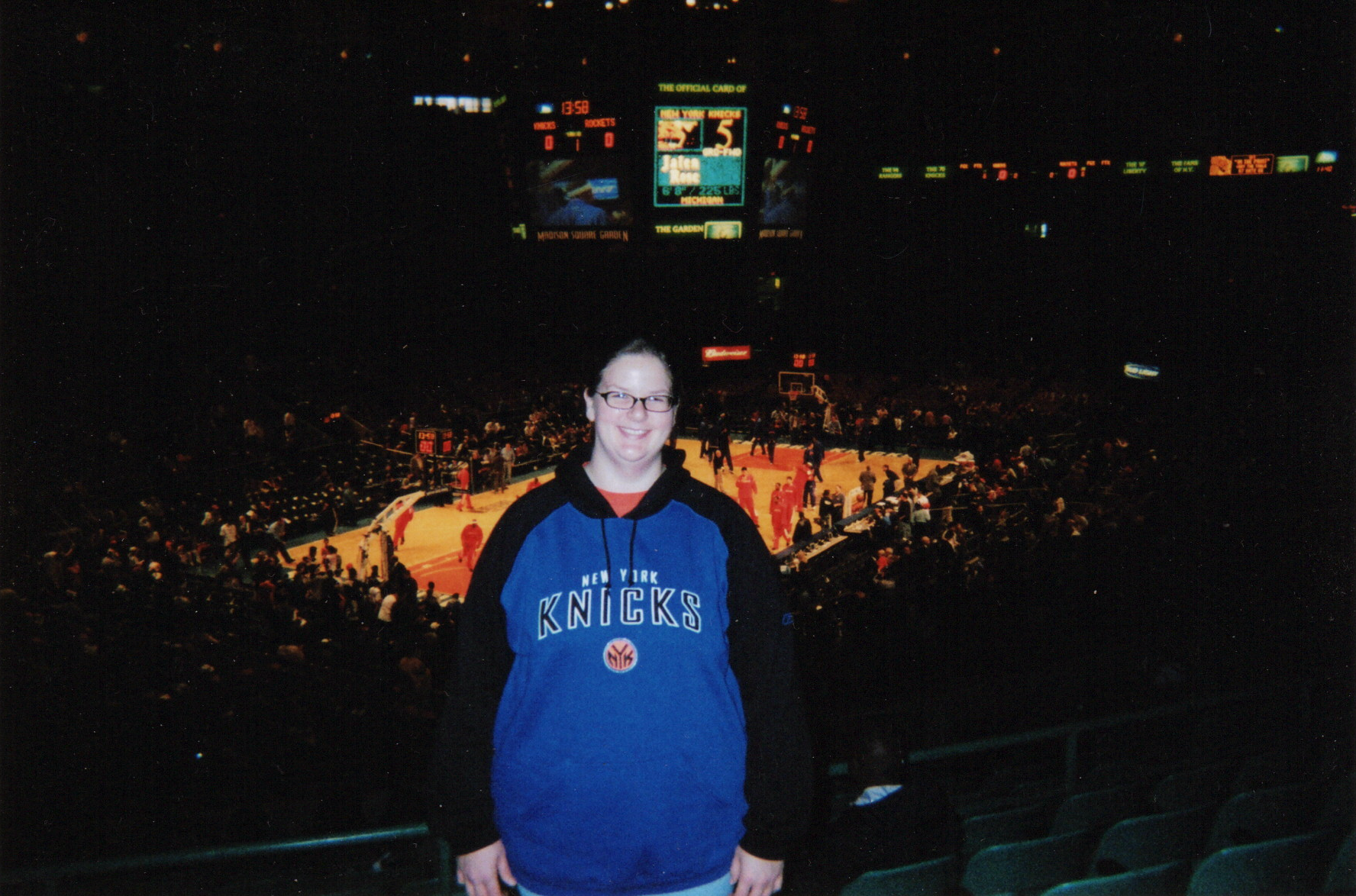 Woman wearing a Knicks jersey standing in front of the basketball court in Madison Square Garden