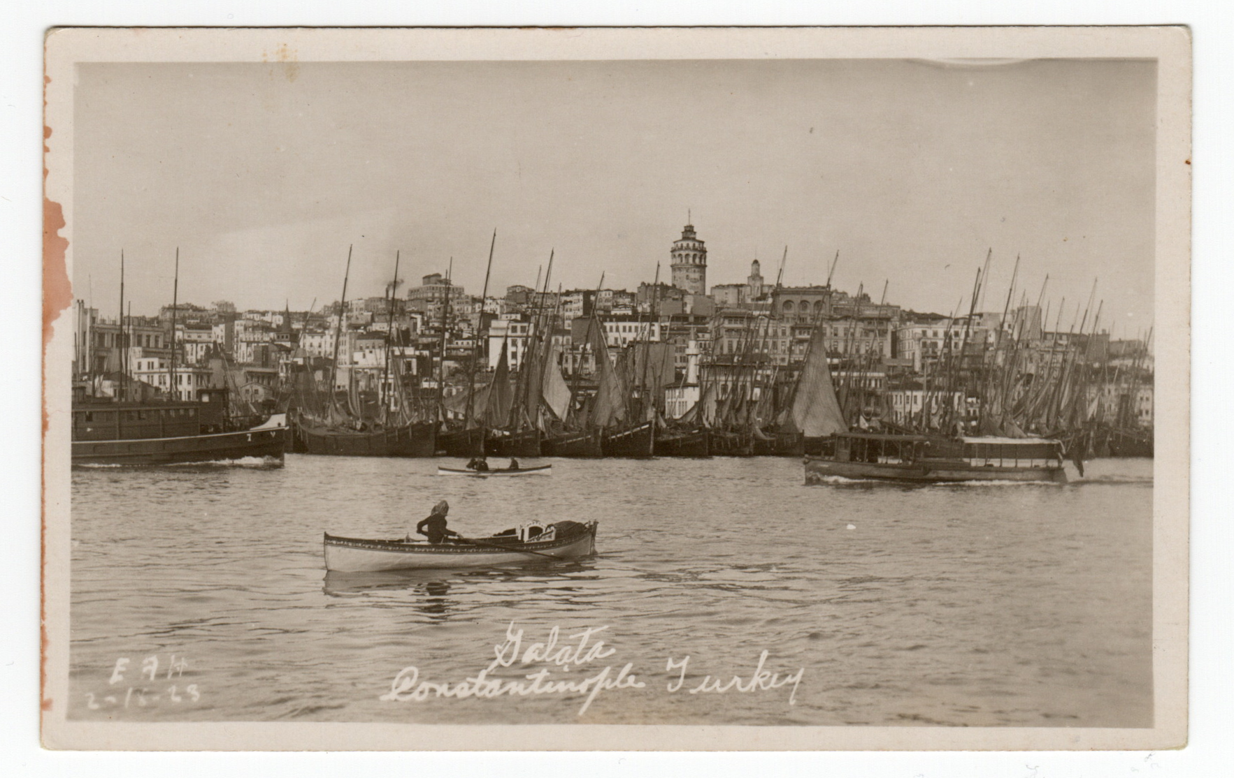 Old postcard showing a person in a boat on the water in front of a busy town