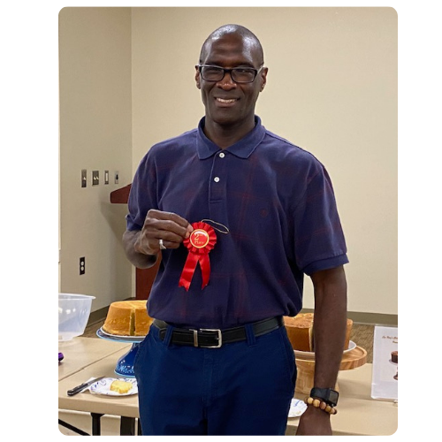 Michael standing in front of pound cakes holding a red ribbon