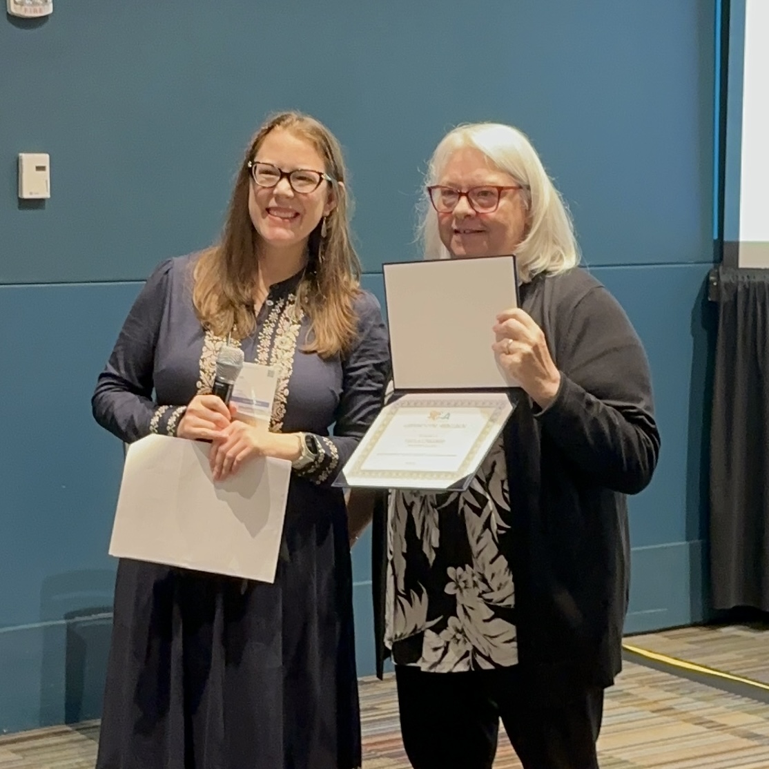 two ladies standing, one holding a certificate