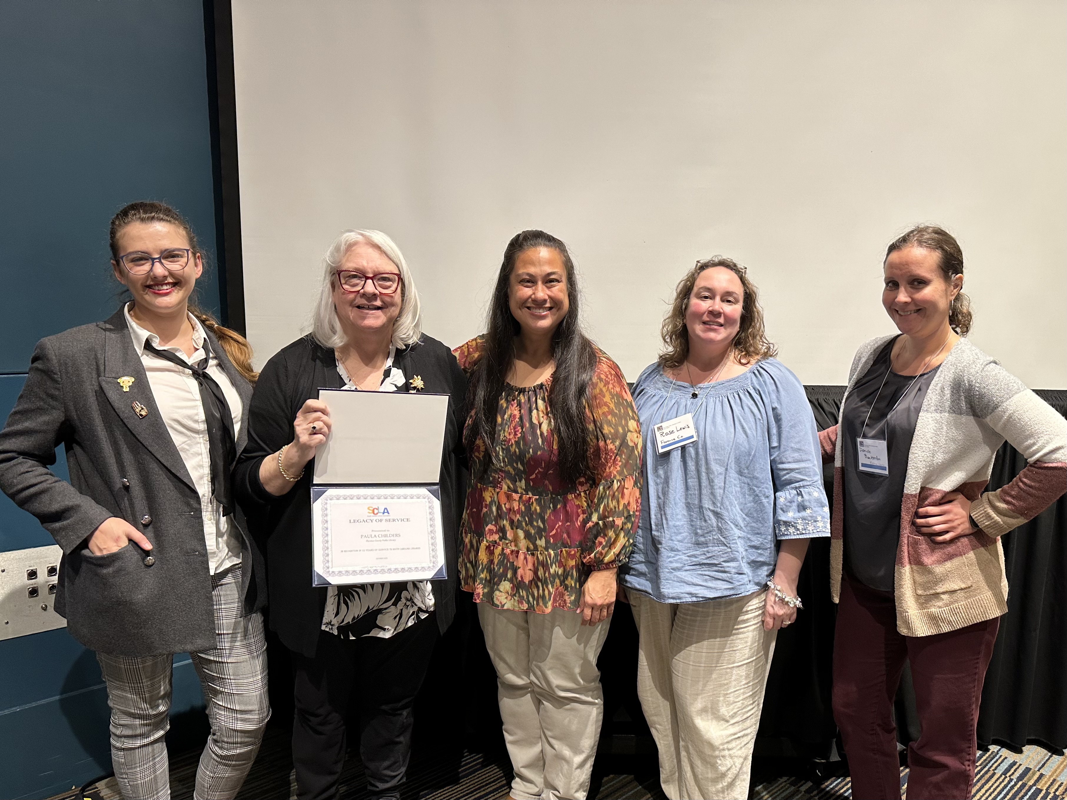 ladies standing in a row, one holding a certificate