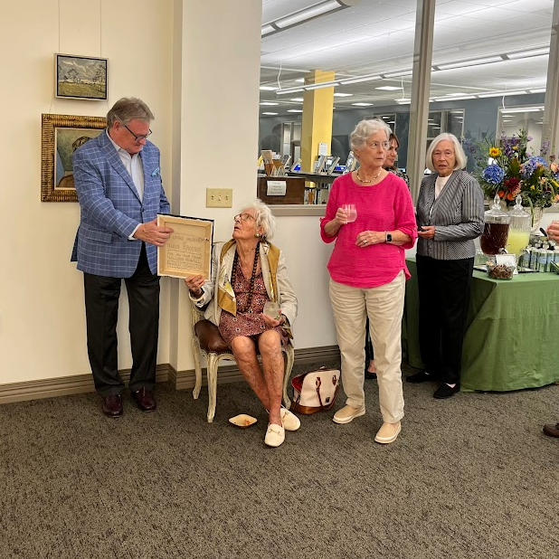 Donor Willson Powell handing a plaque to lady seated in chair