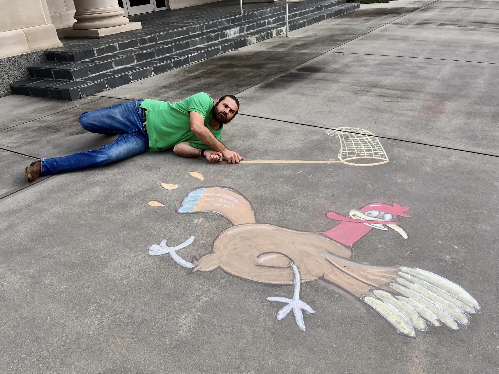 A man laying down next to a chalk drawing for an optical illusion