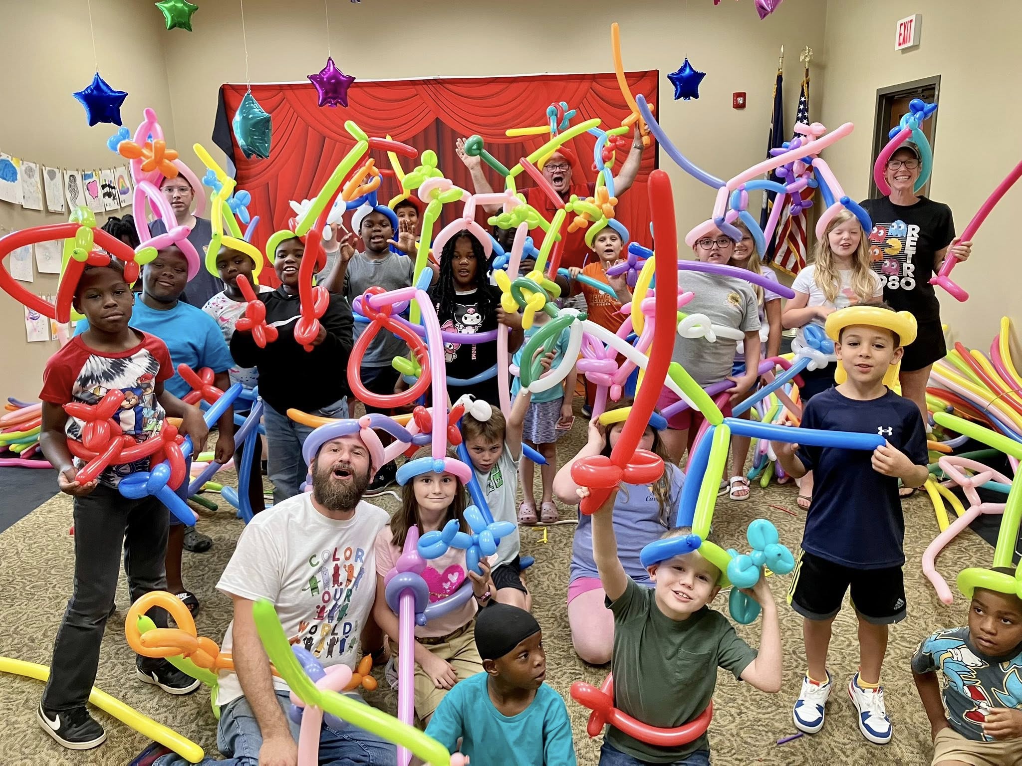A room full of people wearing and waving lots of colorful balloons