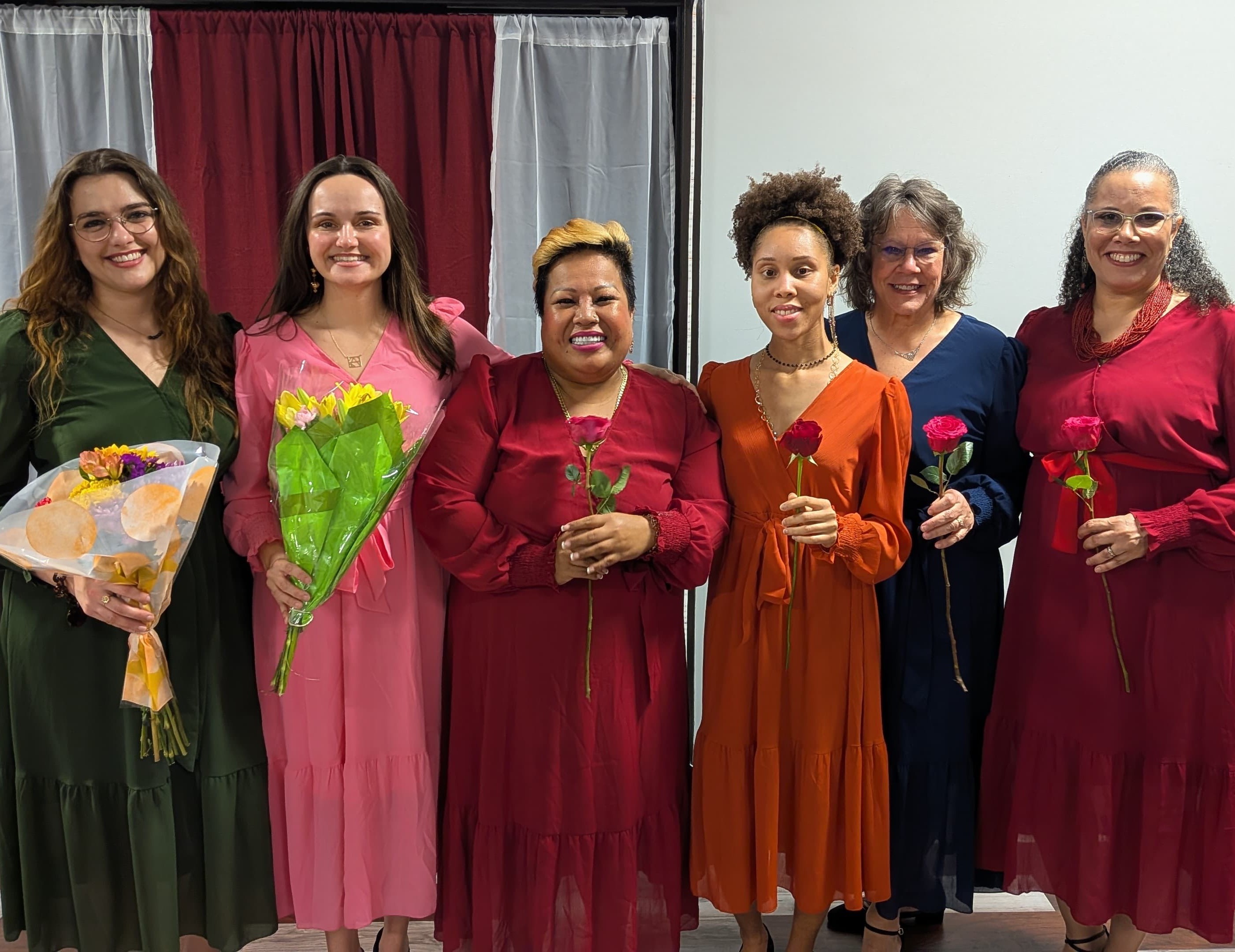 Group of women wearing colorful dresses and holding roses