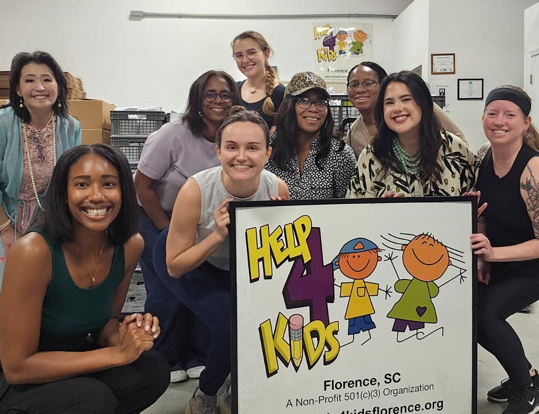 Group of women behind a sign that says Help 4 Kids