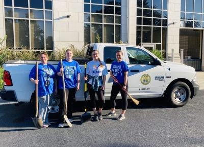 Four ladies standing with brooms and shovels in front of a truck