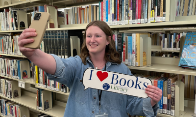 Leah taking a shelfie holding a sign that says I heart books