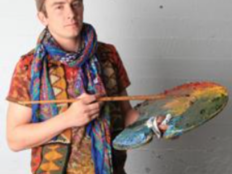 Artist dressed in colorful clothes and hat holding a paint brush and palette