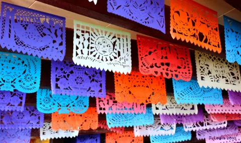Photograph of multiple rows of colorful cut paper banners hanging from a ceiling.