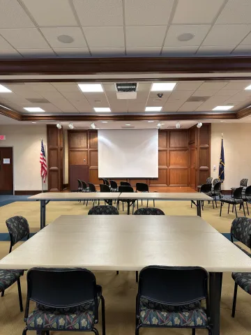 view of Stukes' meeting room with tables, chairs, projector screen, microphone, and dais