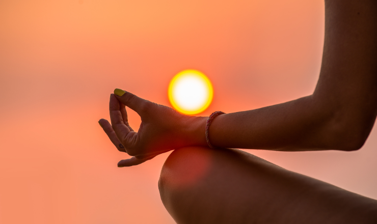 A person sitting in a meditative pose in front of a sunrise