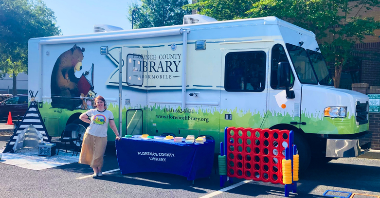 The bookmobile with games set up in front of it and a librarian standing next to it