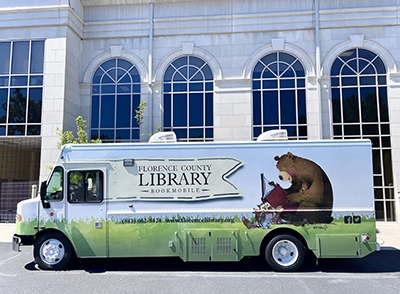 Bookmobile bus out front of the library building with large windows