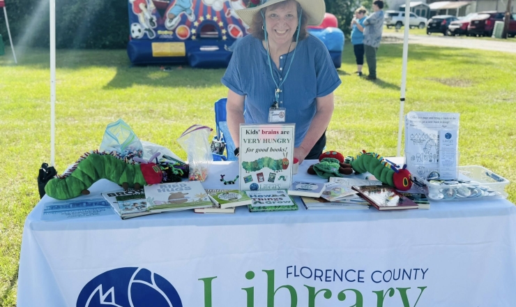 Lady with straw hat behind a table with stuffed caterpillars