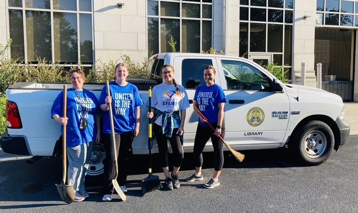 Four ladies standing with brooms and shovels in front of a truck