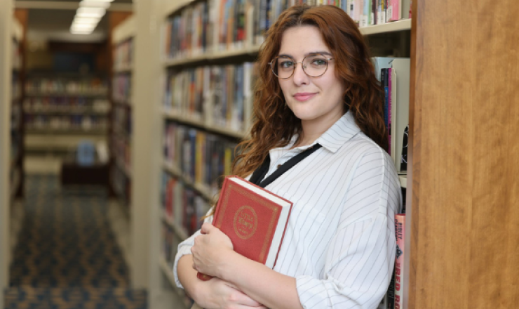 Mikaela holding a copy of Little Women and leaning against a bookcase